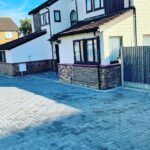 Precision laid grey paving blocks with drainage channels and a red brick retaining wall.