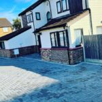 Completed grey block paved driveway with charcoal borders and linear drainage channels.